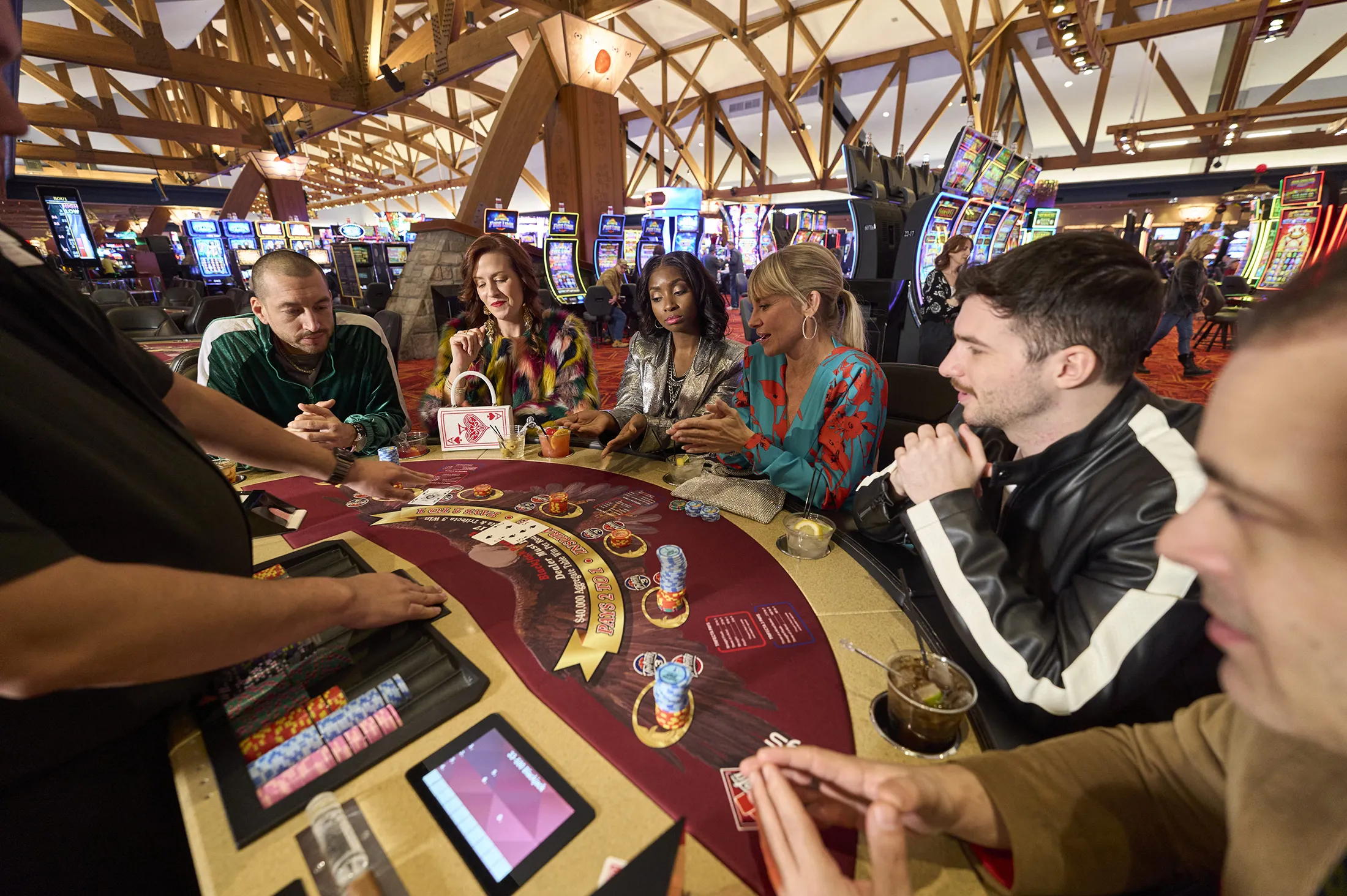 A group of people sitting around a poker table with drinks and poker chips.