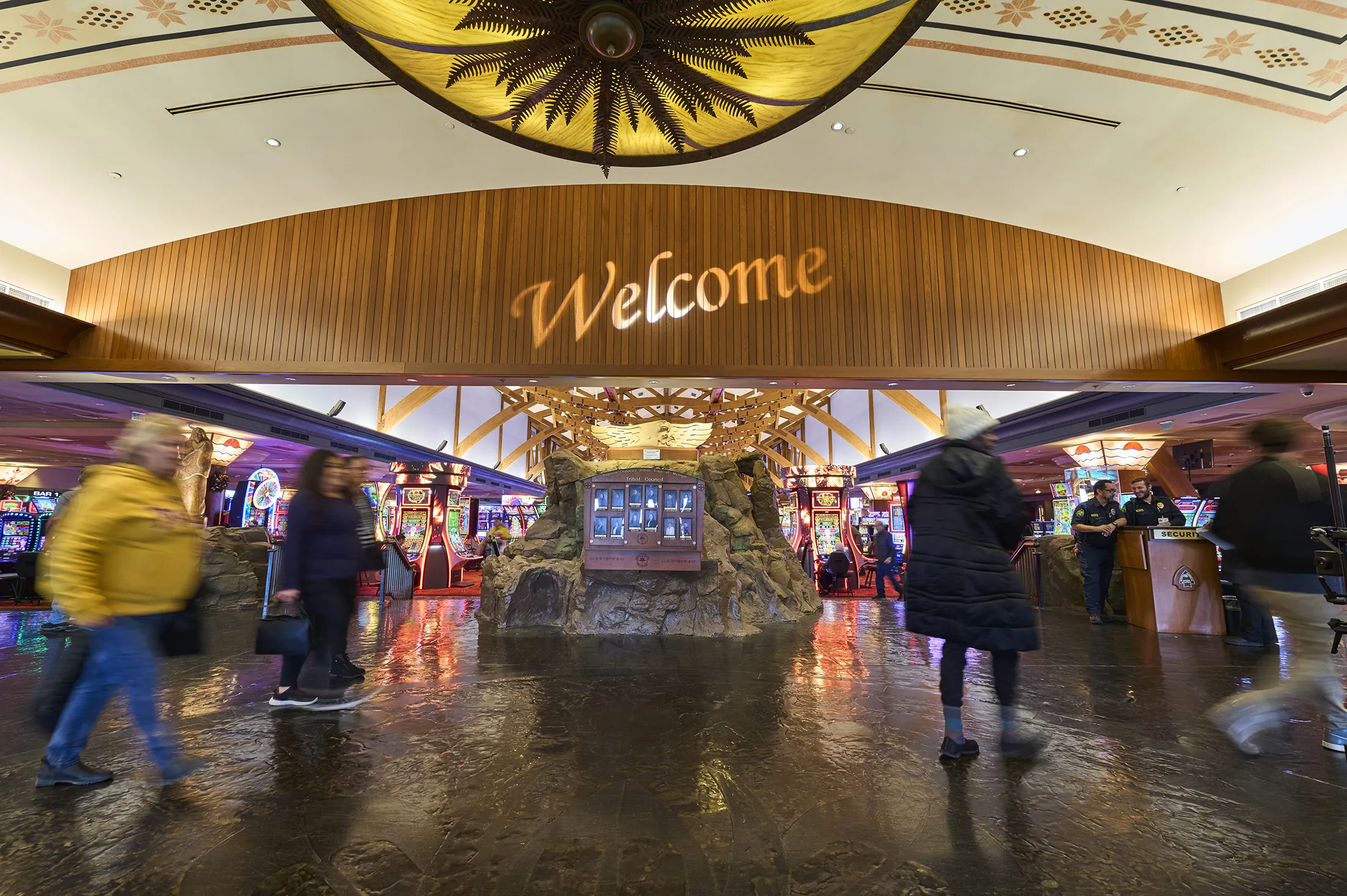 Welcome entrance to casino with lots of slots machines and people walking by.