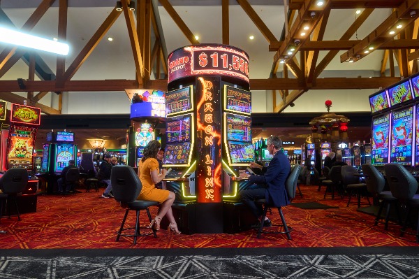 Live casino floor with two people sitting at an electronic slot game